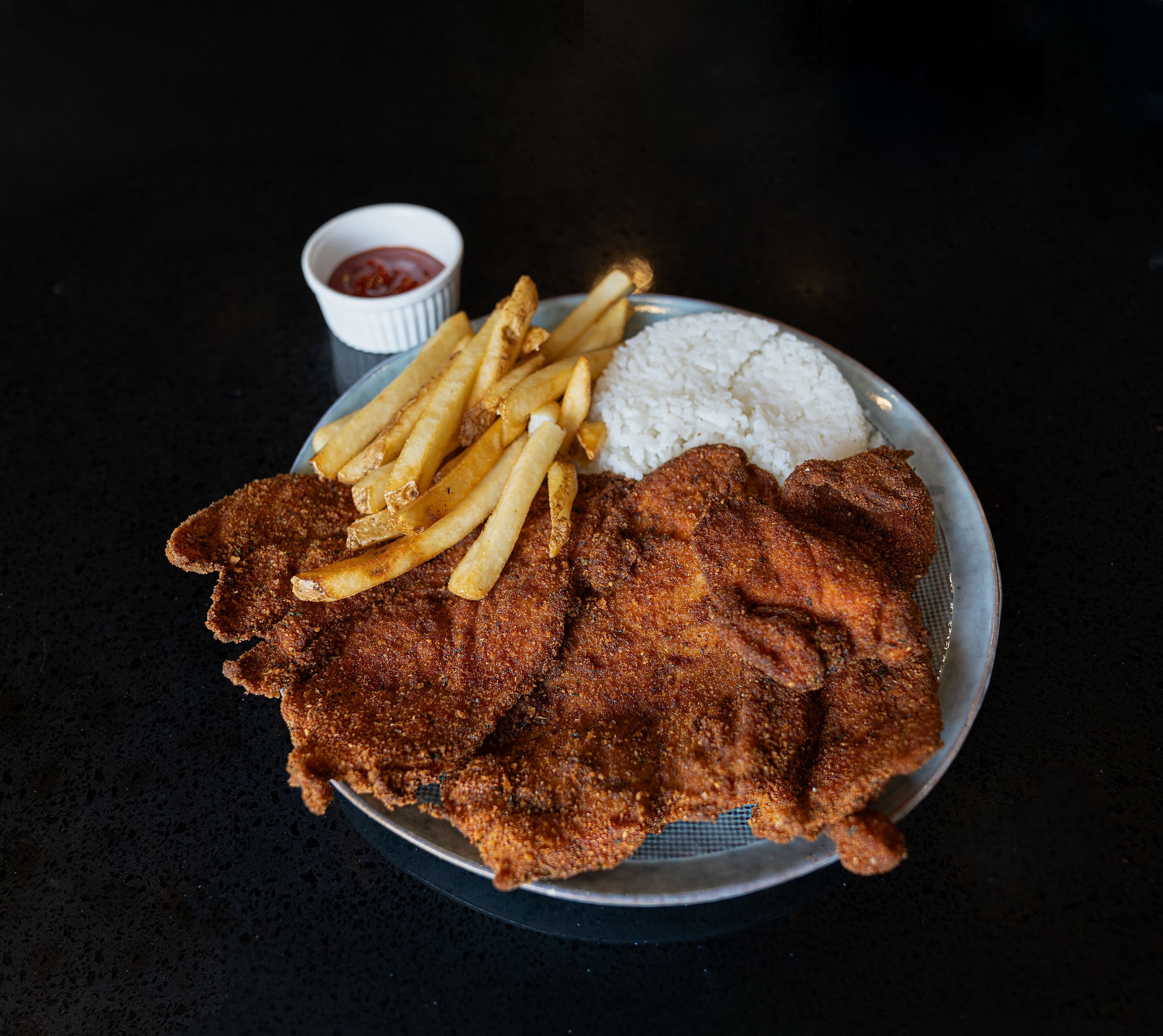 Breaded and fried chicken breast served with rice and fries.