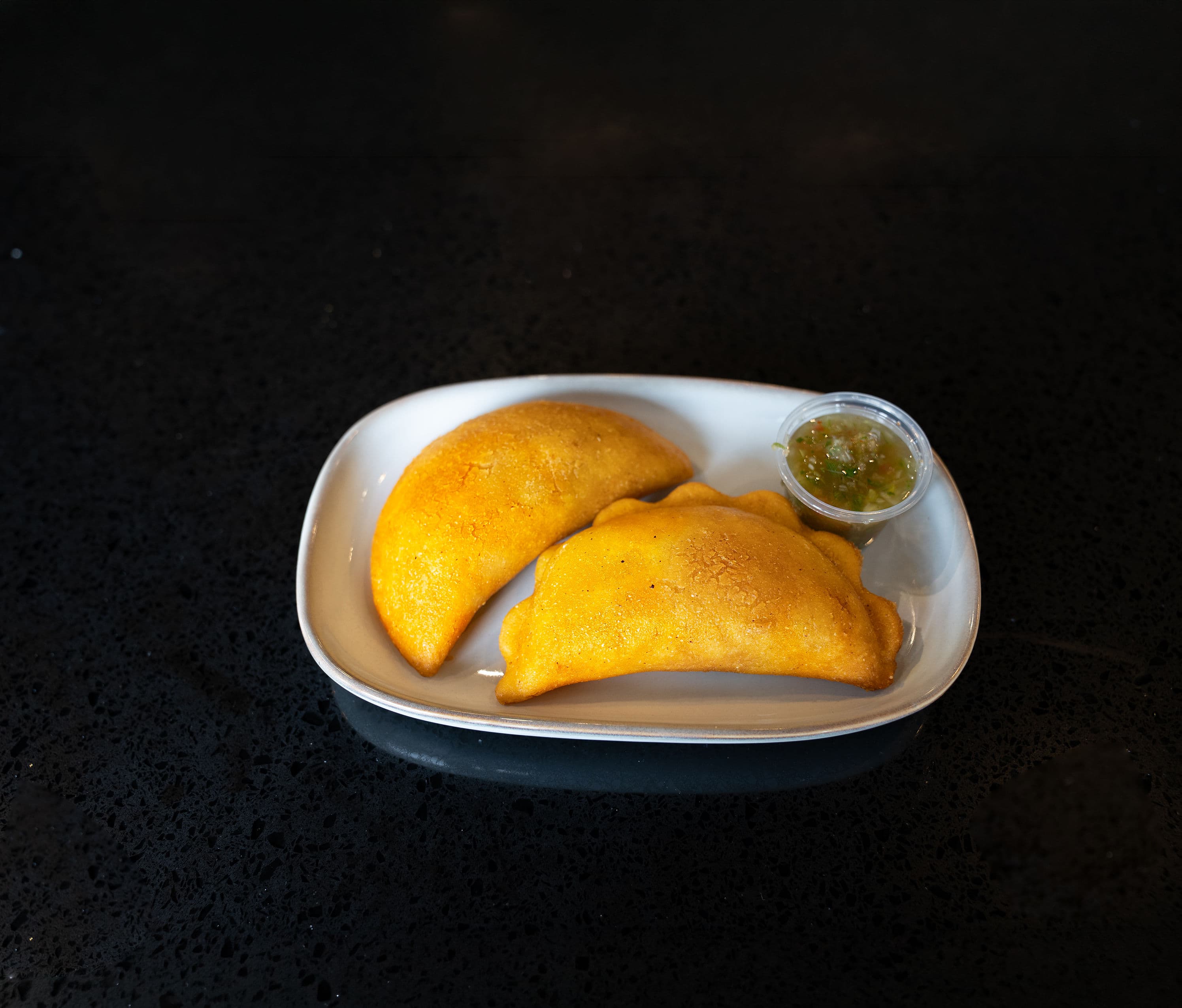 Crispy corn empanadas filled with seasoned beef and potato, served with traditional ají.
